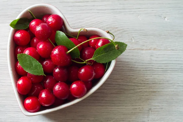 Fresh cherry fruits in heart-shaped bowl on wooden background
