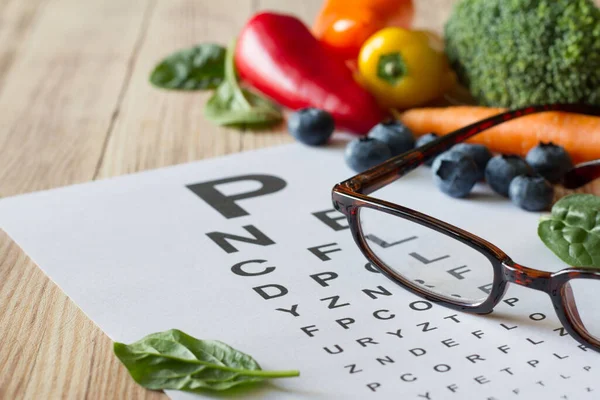 目の健康のための食品 カラフルな野菜や果物 緑豊かな 木製の背景に眼鏡や目のテストチャート コンセプト — ストック写真
