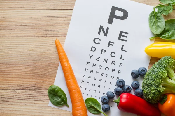 目の健康のための食品 カラフルな野菜や果物 木製の背景にルテインと目のテストチャートが豊富で — ストック写真