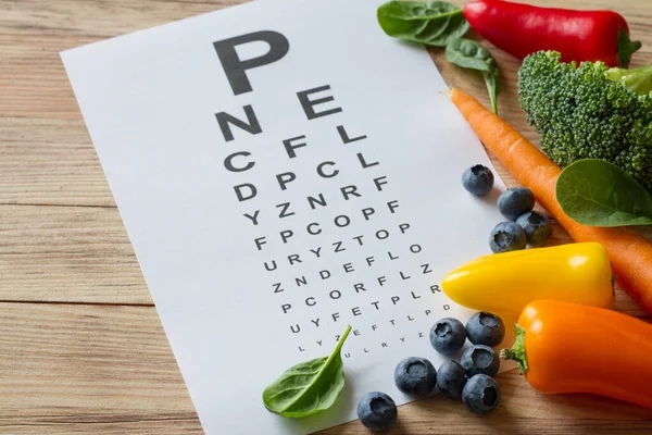 目の健康のための食品 カラフルな野菜や果物 木製の背景にルテインと目のテストチャートが豊富で — ストック写真