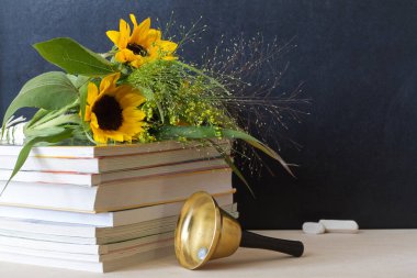 Ayçiçeği buketi, arkaplanda kitap ve çan, okula dönüş konsepti ve Öğretmenler Günü