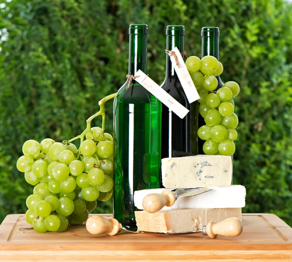 Flasche Wein, Trauben und Käse vor naturgrünem Hintergrund — Stockfoto