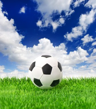 Soccer ball on green grass over dramatic blue sky