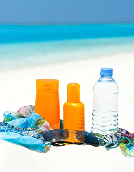 Garrafa de água e creme de proteção solar no fundo da praia — Fotografia de Stock