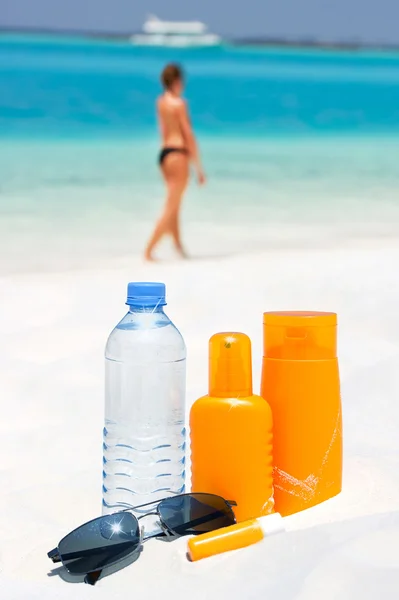 Solglasögon, vatten och solskydd grädde på stranden bakgrund — Stockfoto