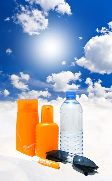 Crème solaire, eau et lunettes de soleil sur le ciel bleu — Photo