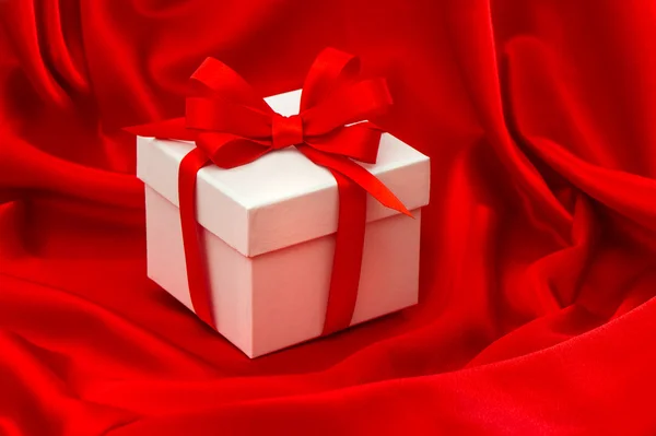 Witte geschenkdoos met strik over rood satijn — Stockfoto