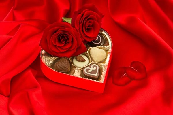 Červené růže s lístky srdce a čokoládové pralinky — Stock fotografie