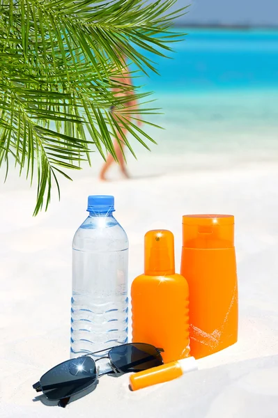 Óculos de sol, água e creme de proteção solar na praia — Fotografia de Stock