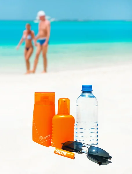 Sun protection cream, water and sun glasses on the beach — Stock Photo, Image