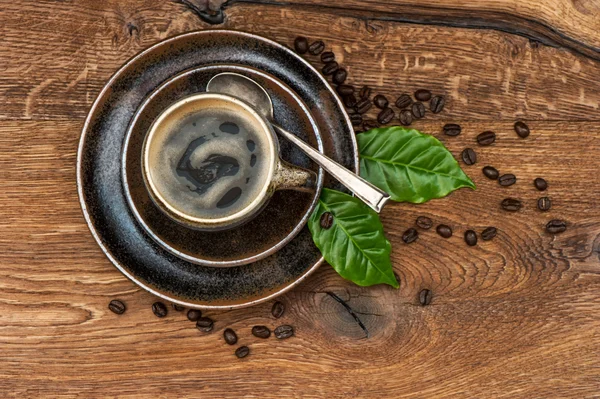 Чашка черного кофе с бобами и листьями на деревянном столе — стоковое фото