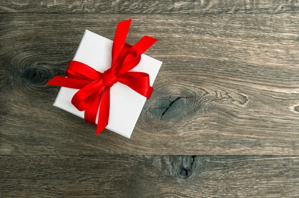 White gift box with red ribbon bow on wooden background — Stock Photo, Image