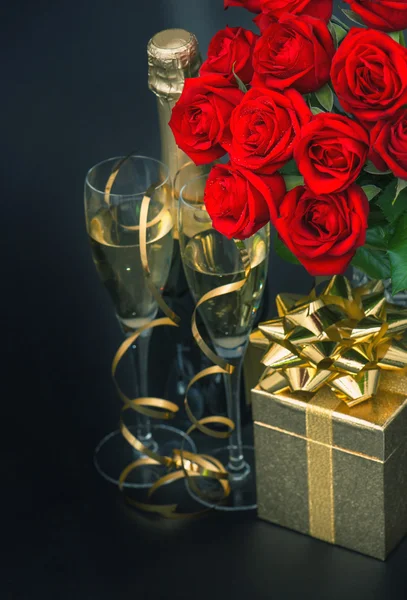 Rosas rojas, caja de regalo dorada y champán sobre fondo negro — Foto de Stock