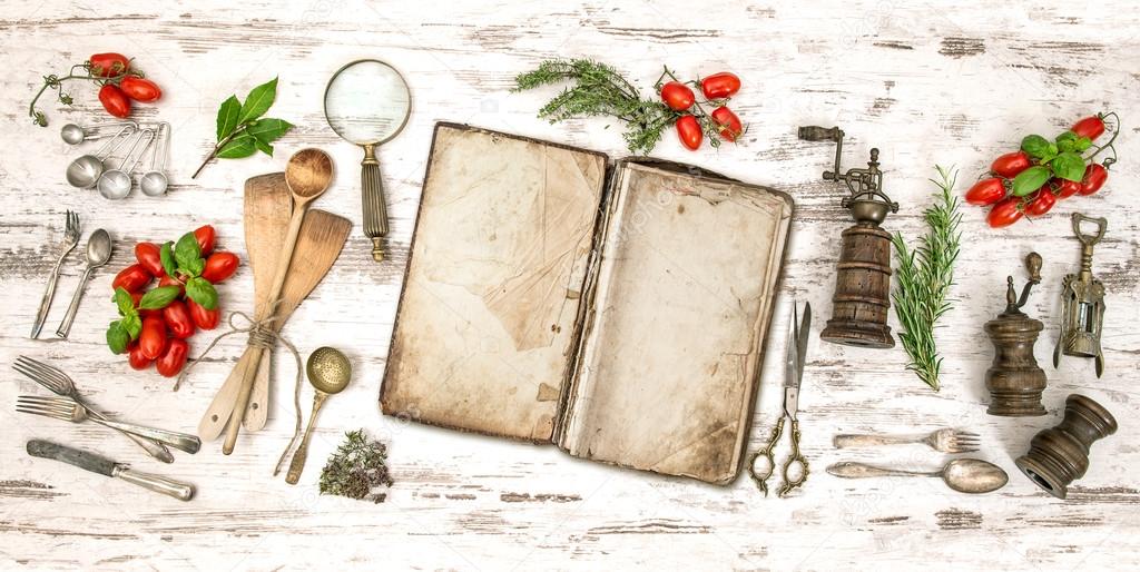 Old cookbook with vegetables, herbs and vintage kitchen utensils