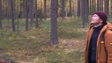 Beyaz adam sırt çantası takıyor ve kozalaklı ormanda yürüyor.