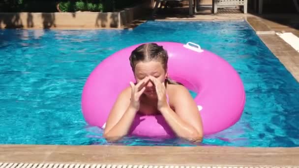 Yüzme havuzunda pembe şişme yüzükle oynayan genç kız. Dalıştan sonra gözlerini ovuşturan bir kız. Yavaş çekim — Stok video