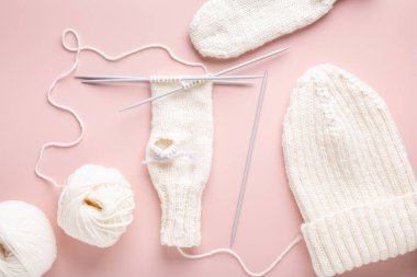 Beyaz yün örgü iğneleri ve pastel pembe arka planda örülmüş şapka. Kadın örgü hobisi. Üst görünüm