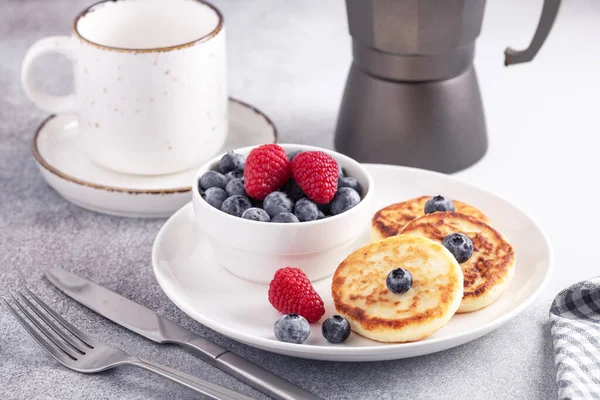 Panqueques de requesón con bayas frescas, taza de café y cafetera en la mesa. Sabrosa comida de desayuno — Foto de Stock