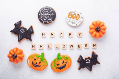 Çeşitli zencefilli kurabiyeler ve beyaz arka planda Mutlu Cadılar Bayramı tahta blokları. Cadılar Bayramı partisi için ev yapımı parlak kurabiyeler.