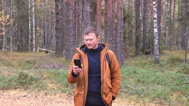 Elinde akıllı bir telefonla beyaz bir adamın portresi var. Ormanda yürürken akıllı telefondan cep telefonu ağı yakalayan bir adam. — Stok video