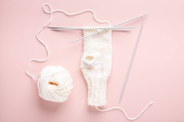 Beyaz yün örgü iğneleri ve pastel pembe arka planda örülmüş şapka. Kadın örgü hobisi. Üst görünüm