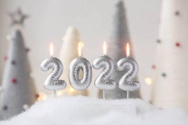 2022 numaralı Noel tebrik kartında gümüş renkli mumlar var. İplik sarılı xmas koni ağaçları ve arka planda çelenk