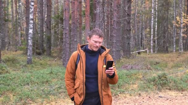 Elinde akıllı bir telefonla beyaz bir adamın portresi var. Ormanda yürürken akıllı telefondan cep telefonu ağı yakalayan bir adam. — Stok video