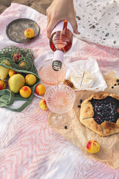 Romantic picnic on the beach at sunset. Womans hand holds a bottle of rose wine and pours wine into a glass