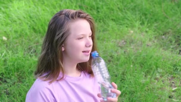 Mädchen trinkt an einem heißen Sommertag sauberes Trinkwasser aus einer Flasche in einem grünen Stadtpark. Nahaufnahme — Stockvideo