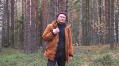 Beyaz bir adam ormanda sırt çantası takıyor. Sırt çantalı bir adam sonbahar ormanında yürüyor.