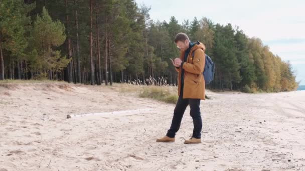 Portret van een blanke man met een smartphone in zijn hand. Een man die een mobiel netwerk vangt op een smartphone tijdens een wandeling in de natuur — Stockvideo