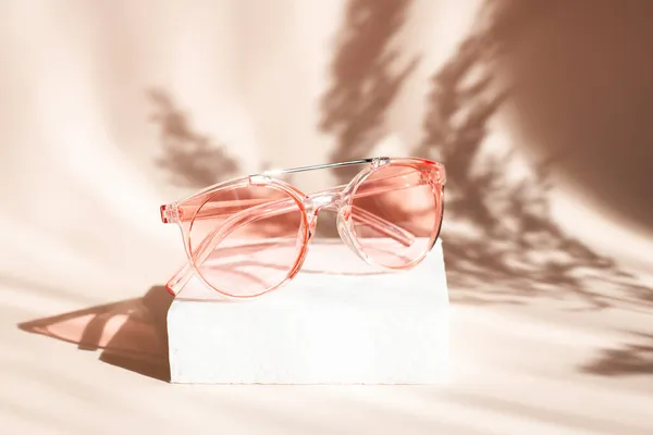 Fashionable pink sunglasses on geometric podium. Pampas grass natural shadows on beige background. Concept of summer sales Royalty Free Stock Photos
