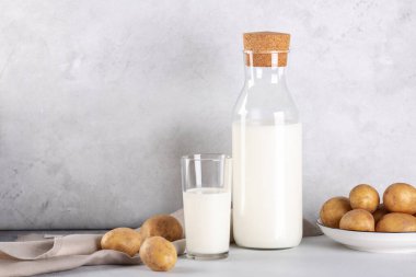 Sütsüz patates, cam ve şişede içecek. Alternatif patates sütü ve patates yumrusu gri masada.