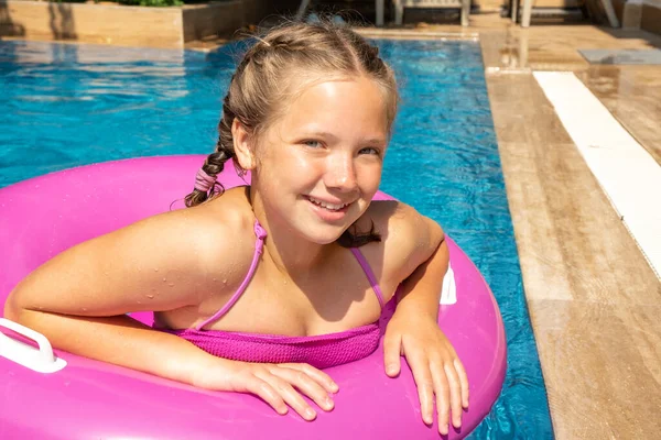 Smiling girl relaxing in swimming pool, floating on pink inflatable ring. Traveling and vacation concept Royalty Free Stock Photos