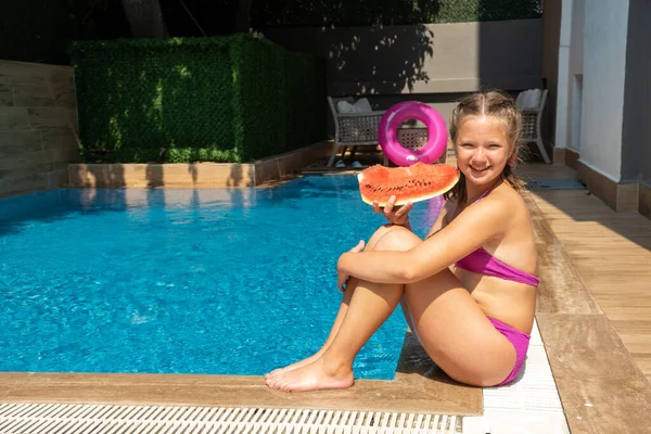 Щаслива мила дівчина, що засмагає біля басейну. Дівчина їсть кавун. Літні подорожі готель відпочинок Ліцензійні Стокові Зображення
