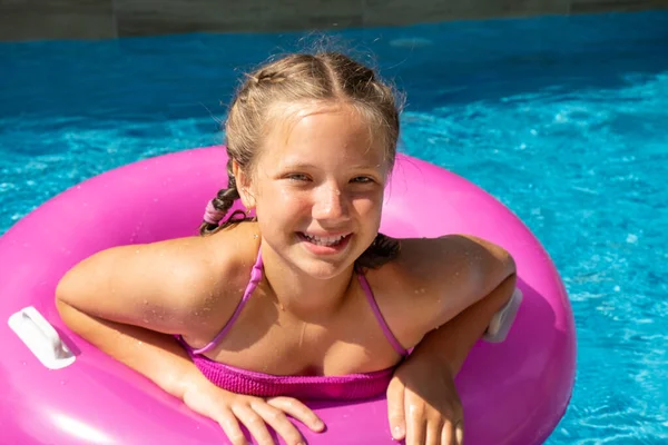 Дівчина-підліток у купальнику плаває на рожевому надувному кільці. Літні подорожі готель відпочинок Ліцензійні Стокові Зображення