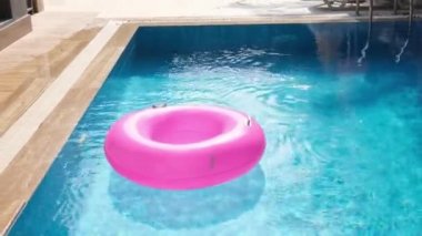 Yüzme havuzunda mavi suyla yüzen pembe şişme yüzük. Seyahat ve tatil kavramı
