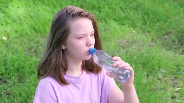 Дівчина п'є чисту питну воду з пляшки в зеленому міському парку в спекотний літній день. Крупним планом — стокове відео