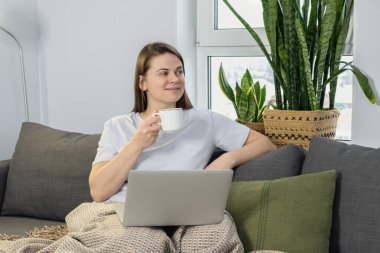 Kupalı genç bir kadın hafta sonu evde dizüstü bilgisayar kullanıyor.