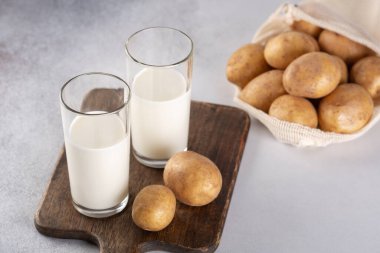 İki şeffaf bardakta vejetaryen sütü. Alternatif patates sütü ve patates yumrusu gri masada.
