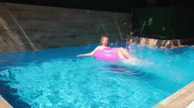 Turkuaz suyla yüzme havuzunda dinlenen bir kız. Pembe şişme yüzükle yüzen kız, ayaklarıyla su sıçratıyor. Seyahat ve tatil kavramı