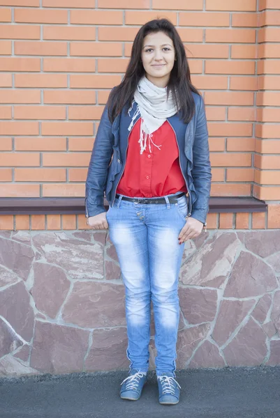 La muchacha joven se para sobre el fondo por la pared de ladrillo. —  Fotos de Stock