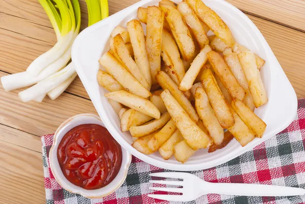 Batatas fritas com ketchup e cebolas em uma mesa de madeira . — Fotografia de Stock