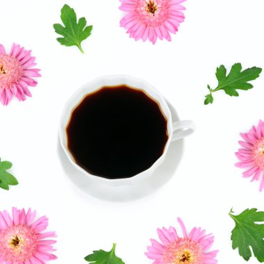 Beyaz arka planda izole edilmiş pembe kasımpatı çiçekleri çerçevesinde bir fincan kahve..
