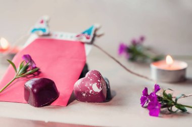 Kalp şeklinde çikolatalar, kırmızı zarf ve ahşap bir masanın üzerinde çiçekler, yakın çekim.
