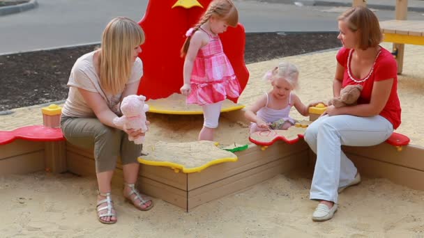 Madri guardando la loro figlia che gioca in scatola di sabbia — Video Stock