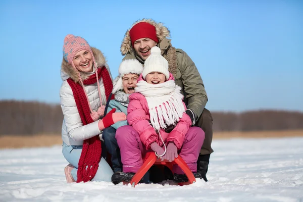 Happy kids sitting on sledge with their parents — Stock Photo, Image