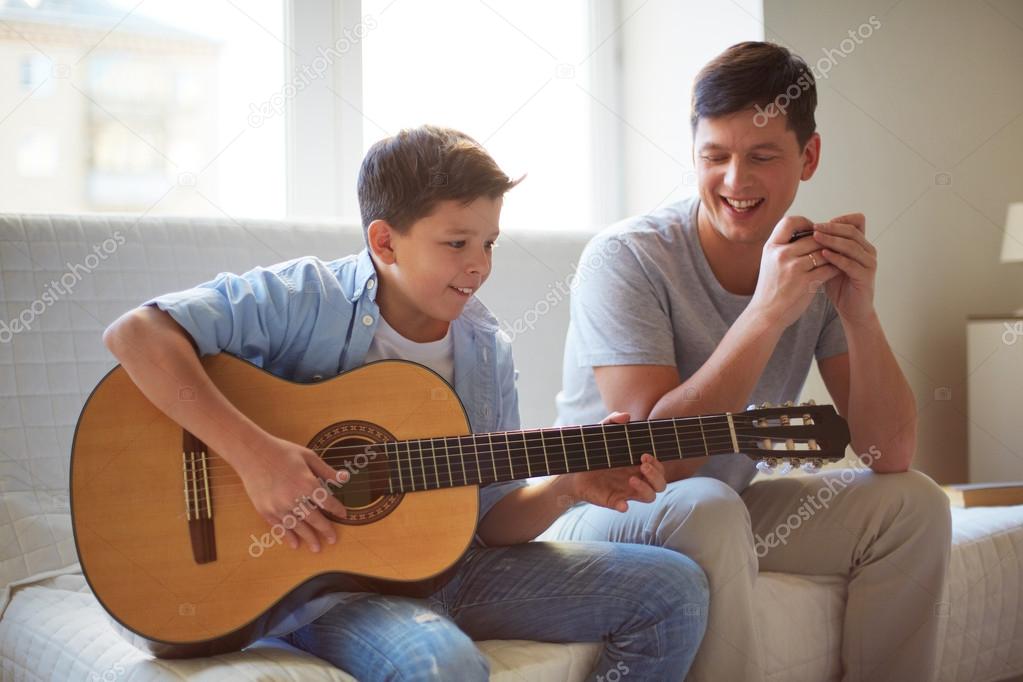 Boy playing guitar with father