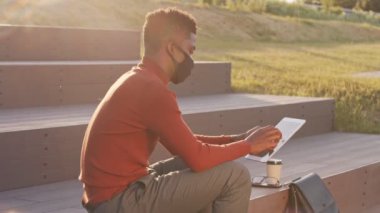 Güneşli bir günde şehir parkındaki merdivenlerde dijital tablet üzerinde çalışan Afro-Amerikalı genç iş adamının yavaş çekimleri.