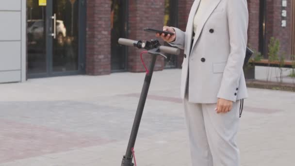夏のダウンタウンでの輸送のための電動スクーターを使用してエレガントなパンツのスーツで自信を持って白人のビジネス女性の傾きの遅いショット — ストック動画